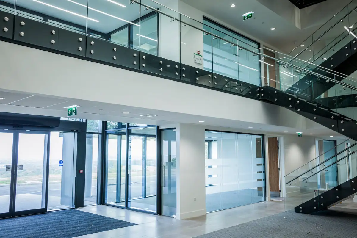 Bright modern office entrance with glass doors, a glazed balcony and a black steel staircase