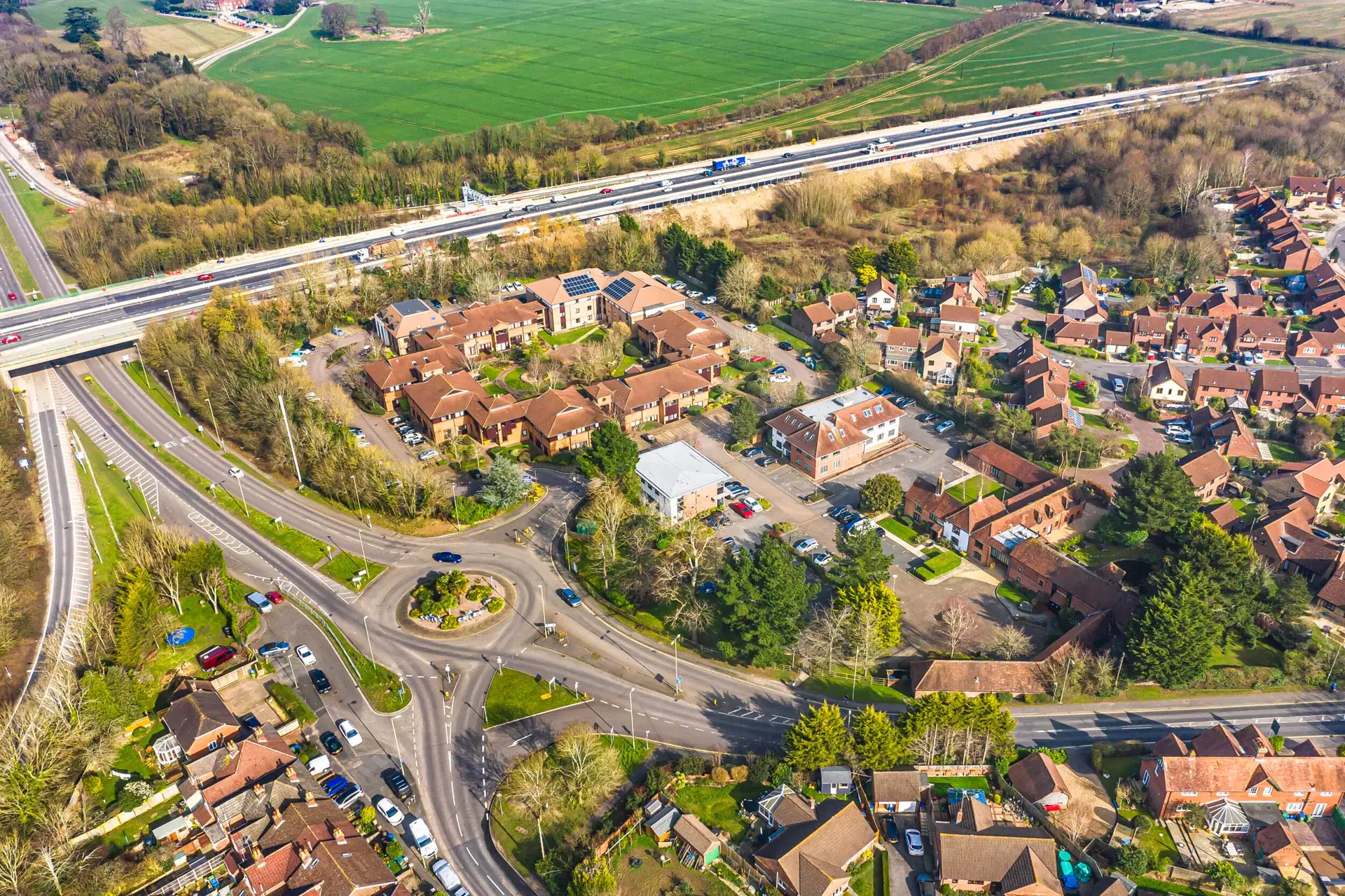 Aerial view of a motorway junction and roundabout beside a residential area and green fields