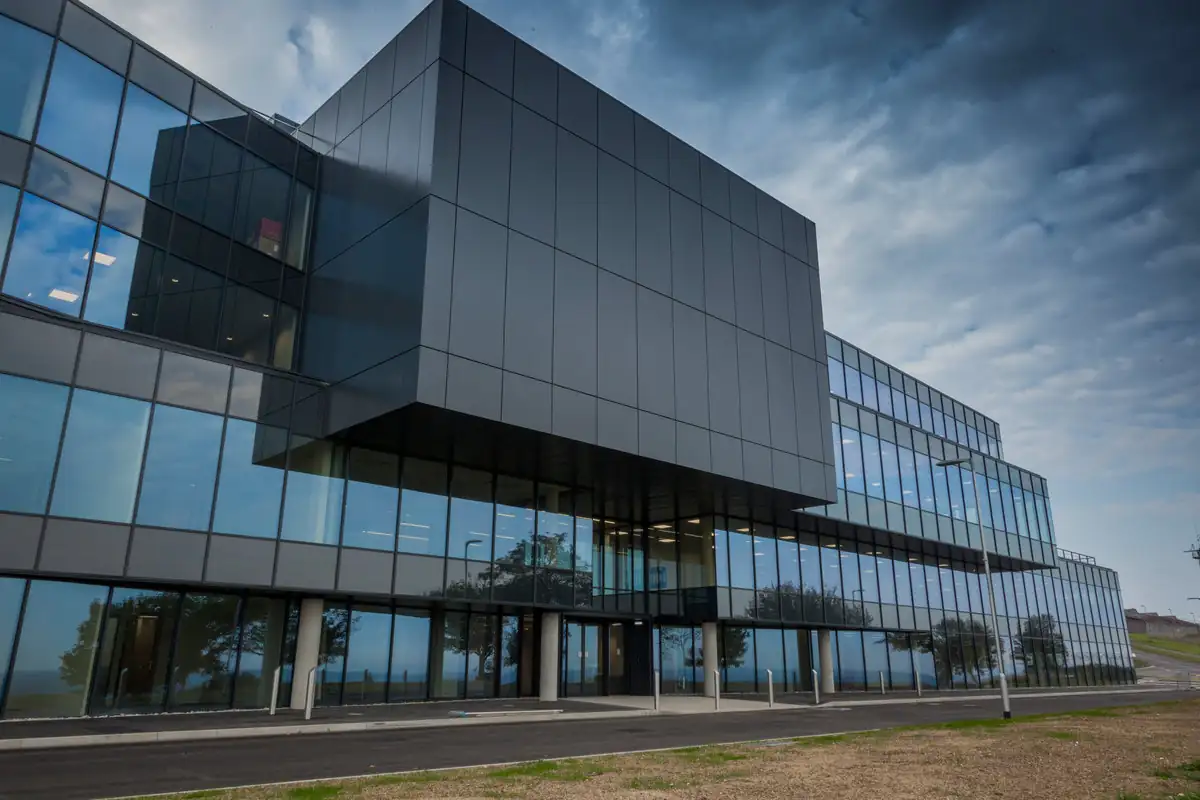 Modern glass and dark-panel office building under a dramatic cloudy sky