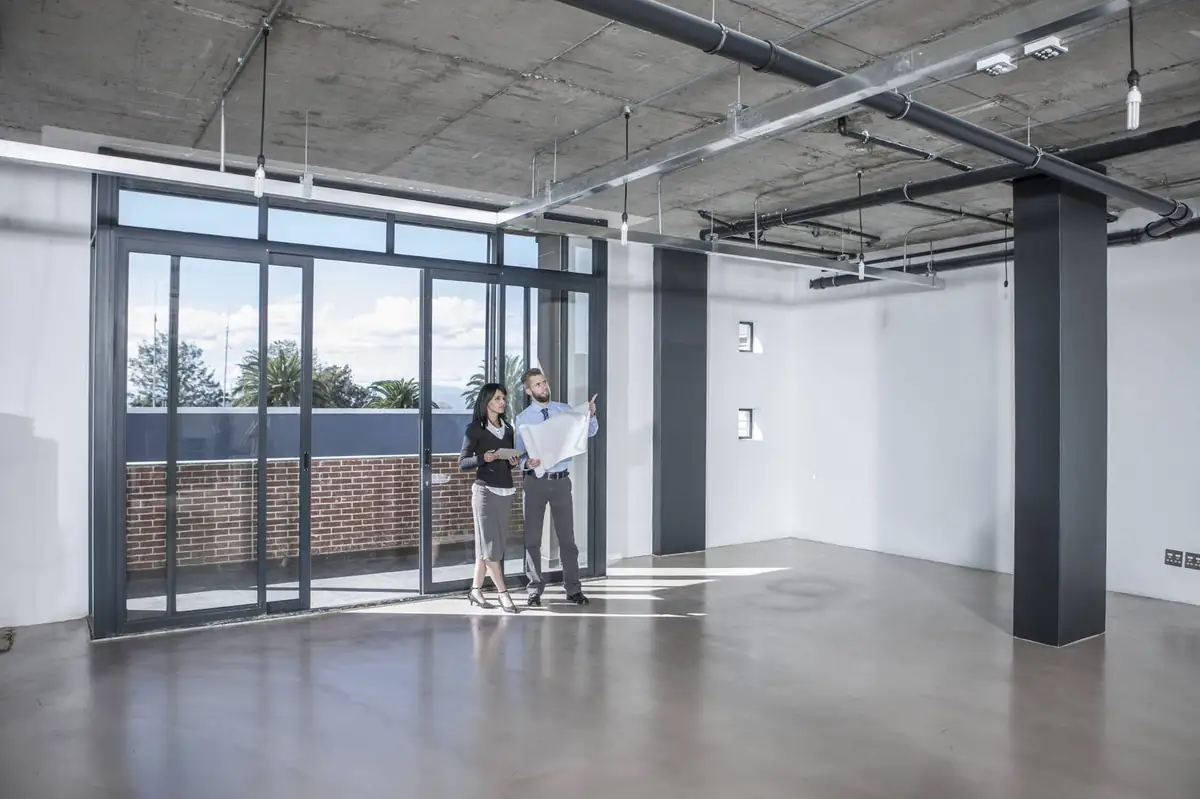 Two people reviewing plans in an empty open-plan office unit with large glass doors