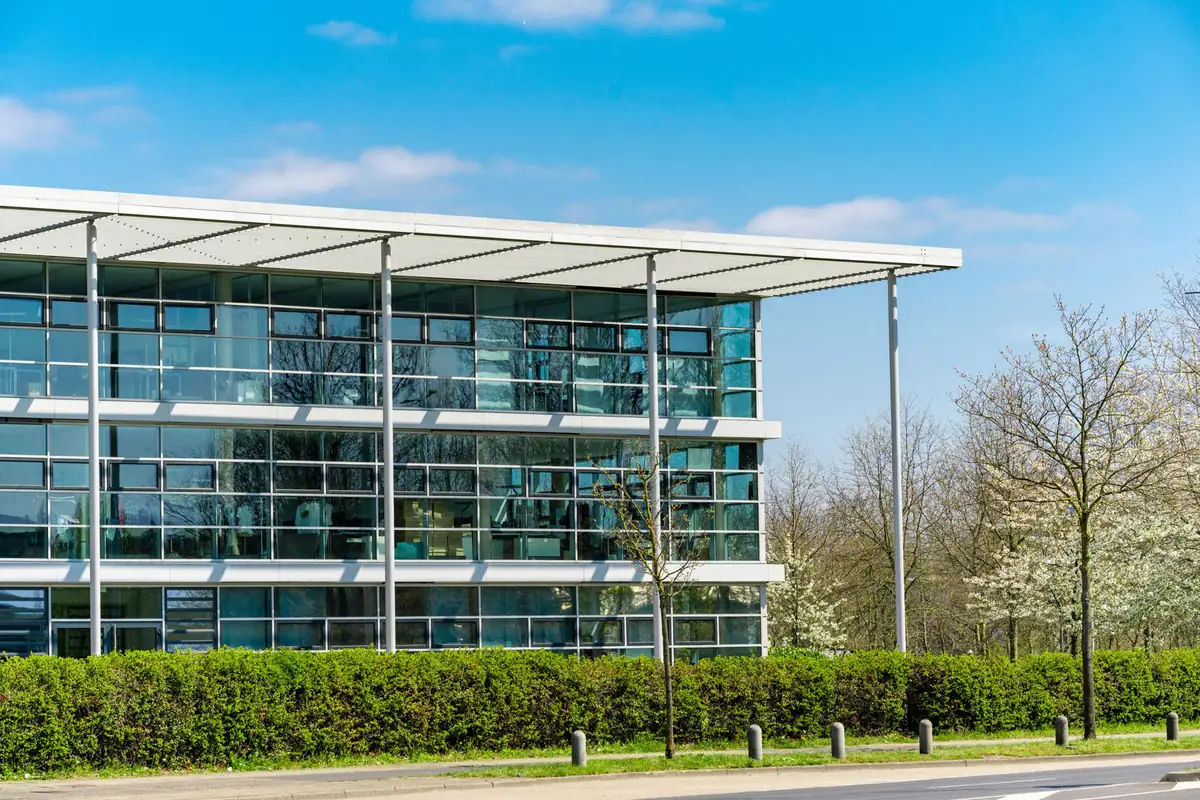 Modern glass-fronted office building beside a hedge and blossom trees