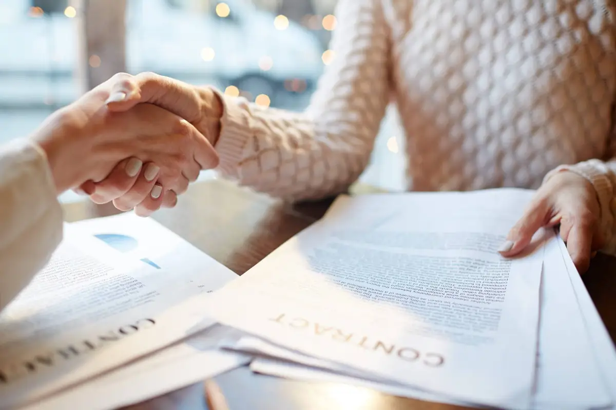 Two people shaking hands over contract documents