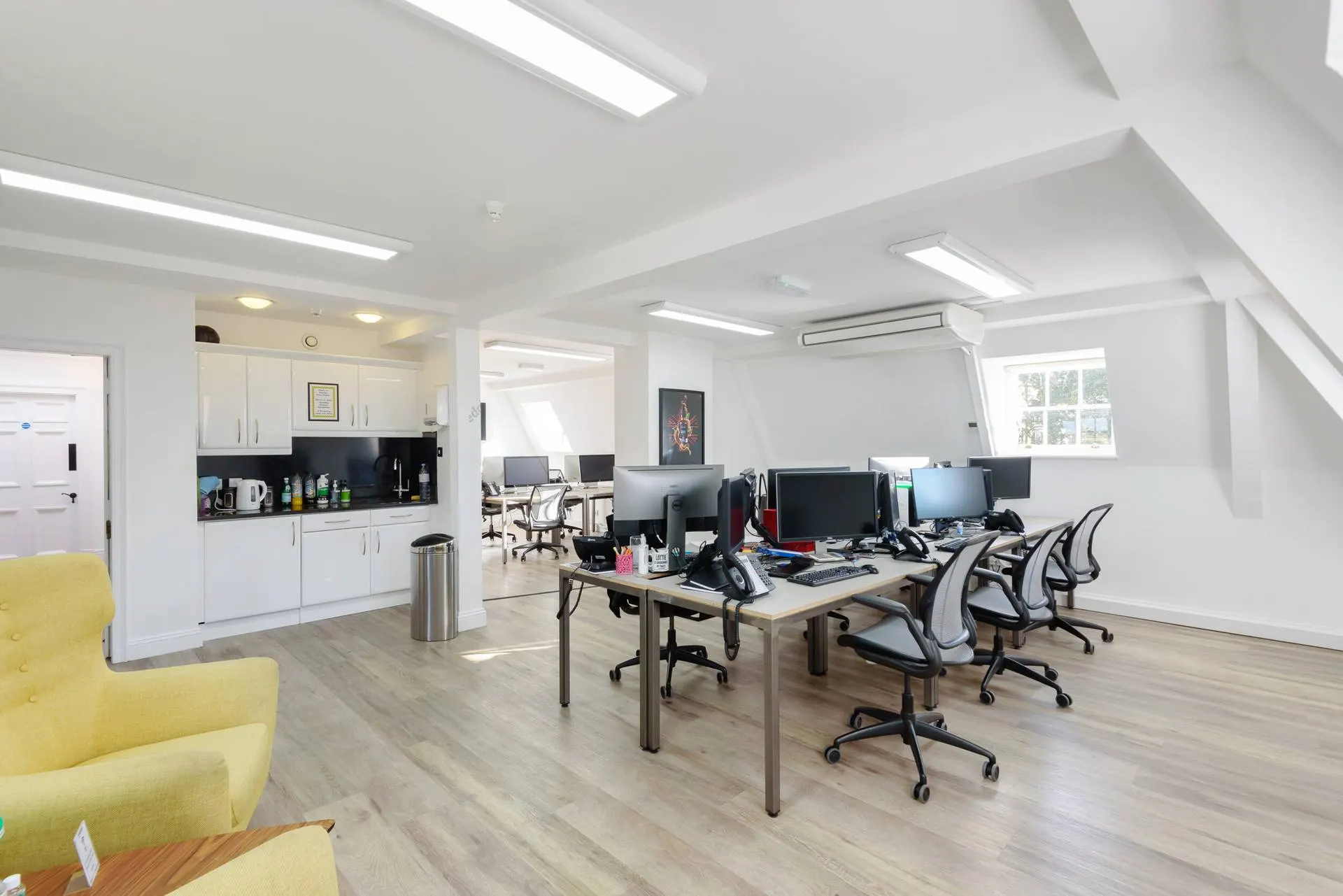 Bright open-plan office with desks, office chairs, a kitchenette and a yellow armchair