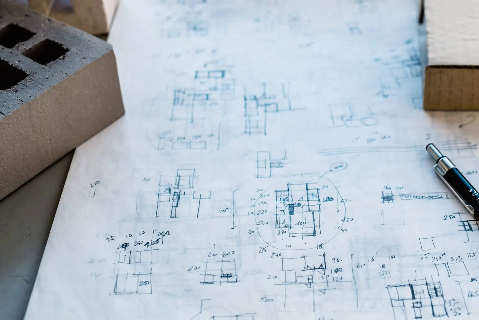 Hand-drawn architectural floor plan sketches on paper beside a breeze block and a pen