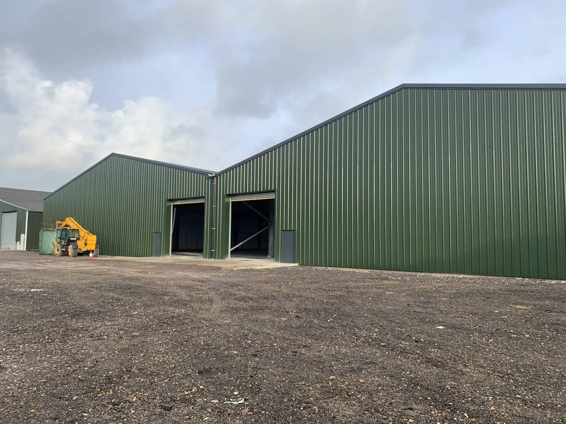 Large green steel-clad industrial building with open doors and a gravel forecourt