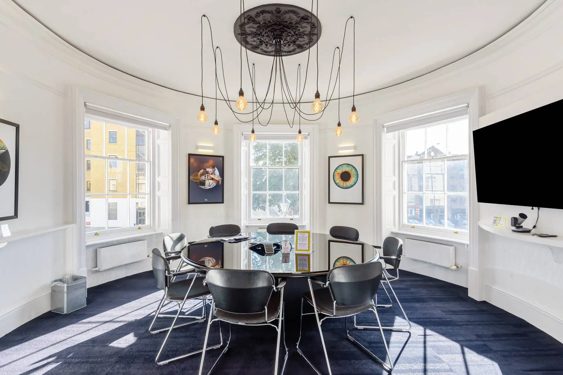 Circular boardroom with a round meeting table, chairs, a pendant light and tall windows