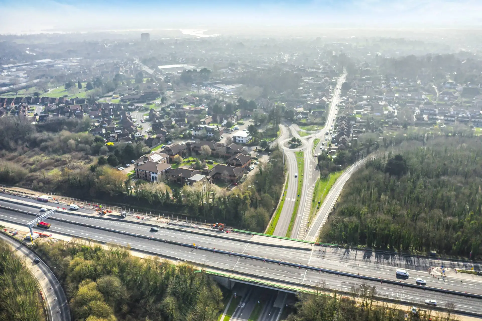 Aerial view of a motorway running past woodland and a residential area