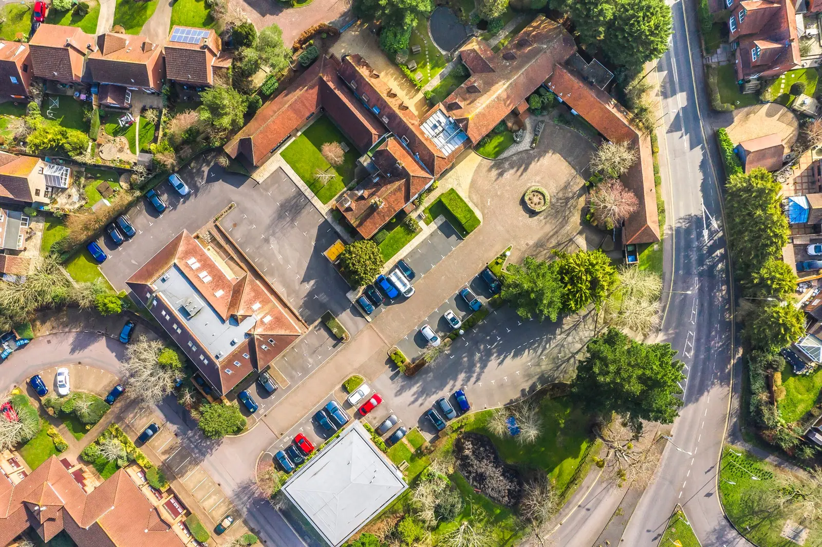 Aerial view of a residential area with red-roofed buildings, gardens and a car park