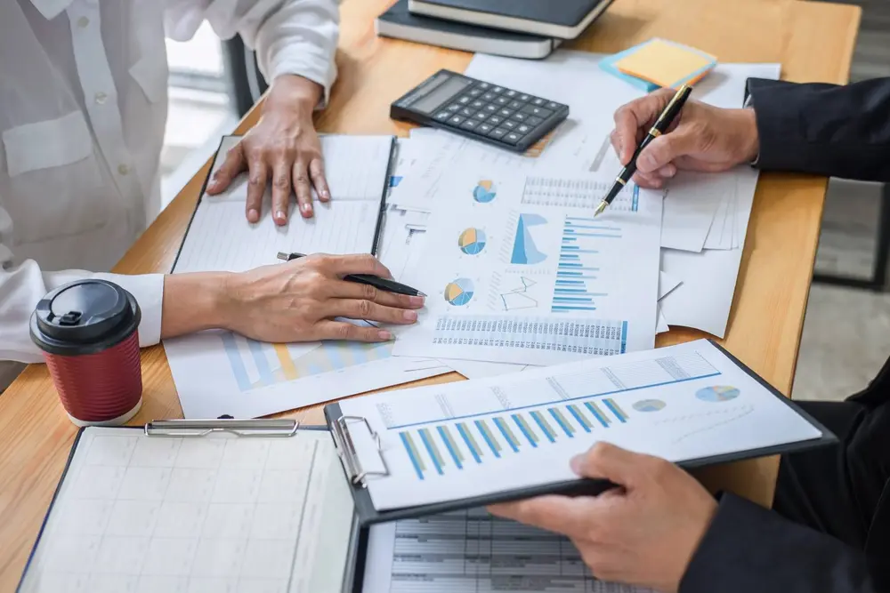 Hands reviewing financial charts and paperwork with a calculator on a desk
