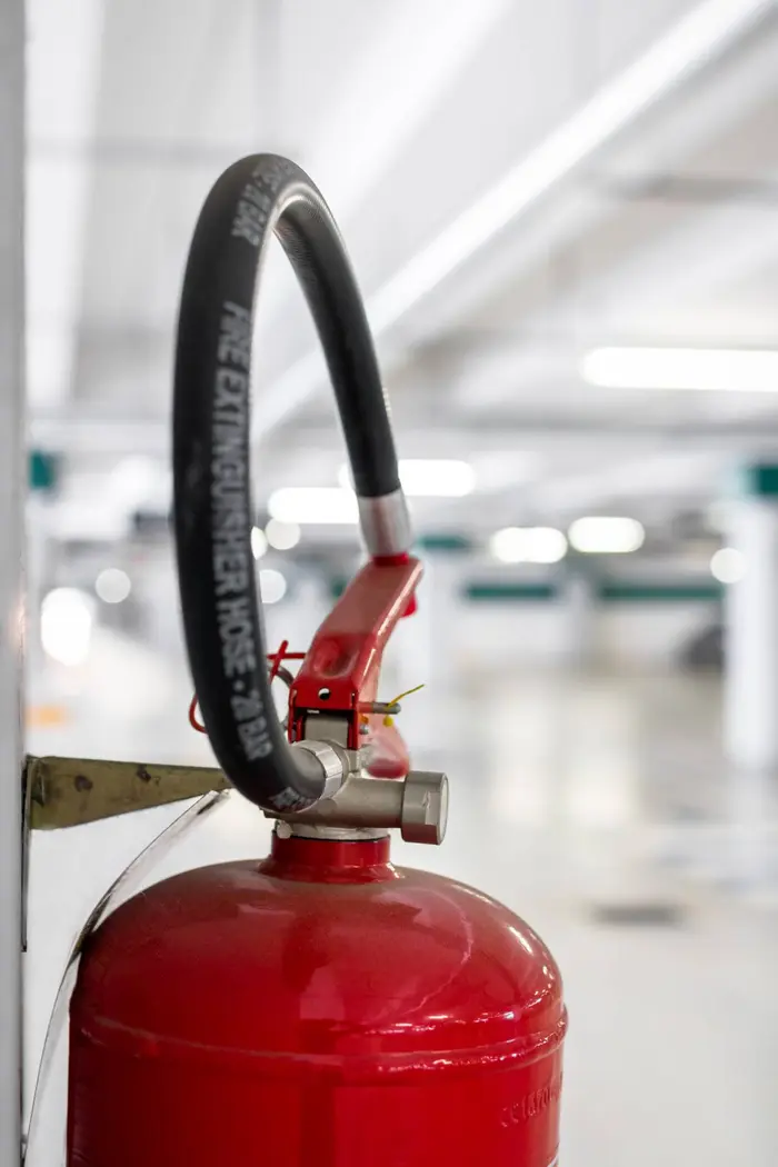 Red fire extinguisher mounted on a wall in a car park