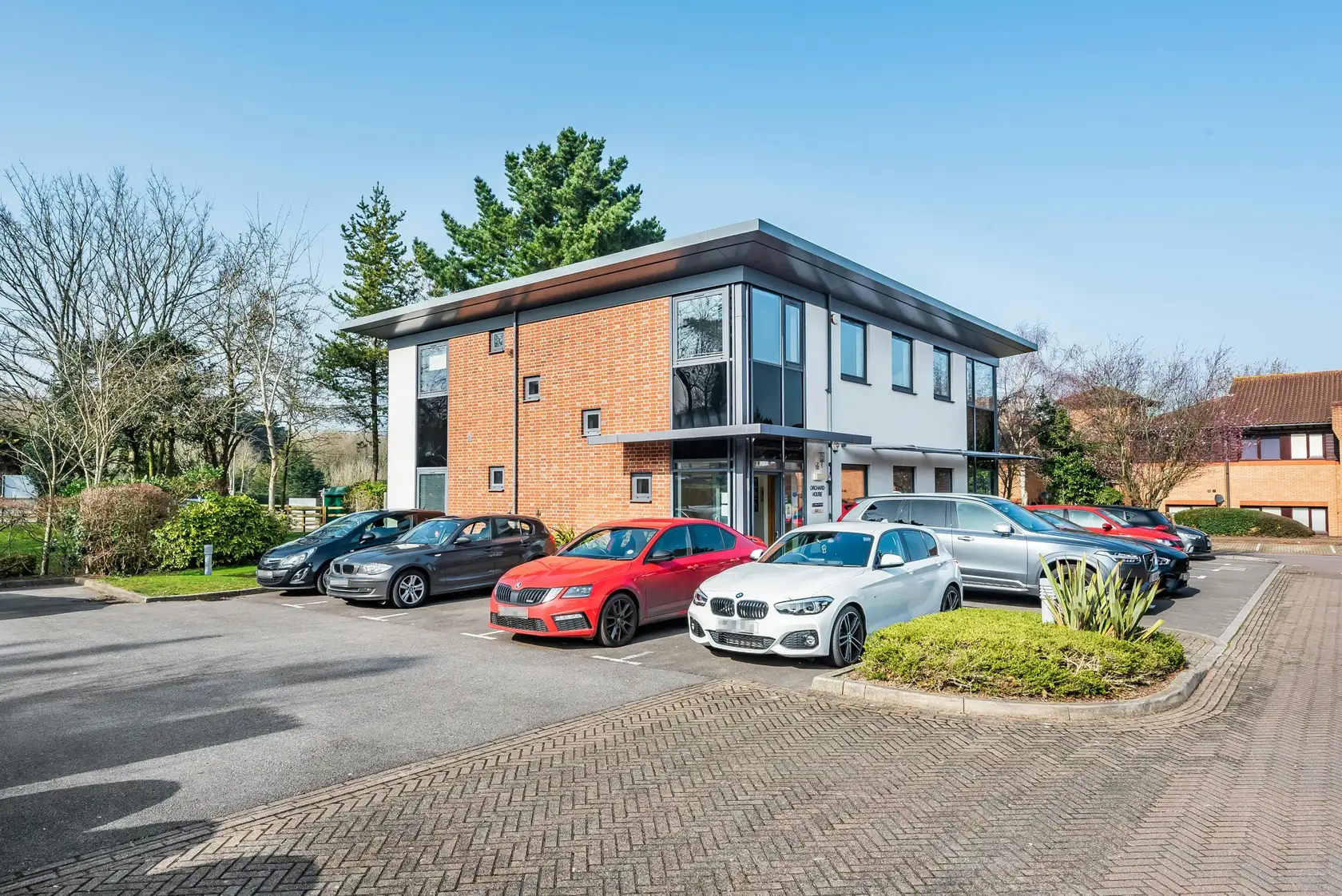 Brick and glass office building with cars parked on a paved forecourt