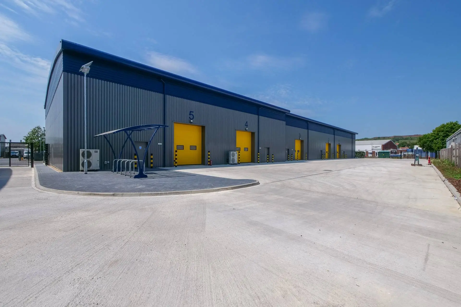Modern industrial unit with grey cladding, yellow loading doors and a concrete forecourt