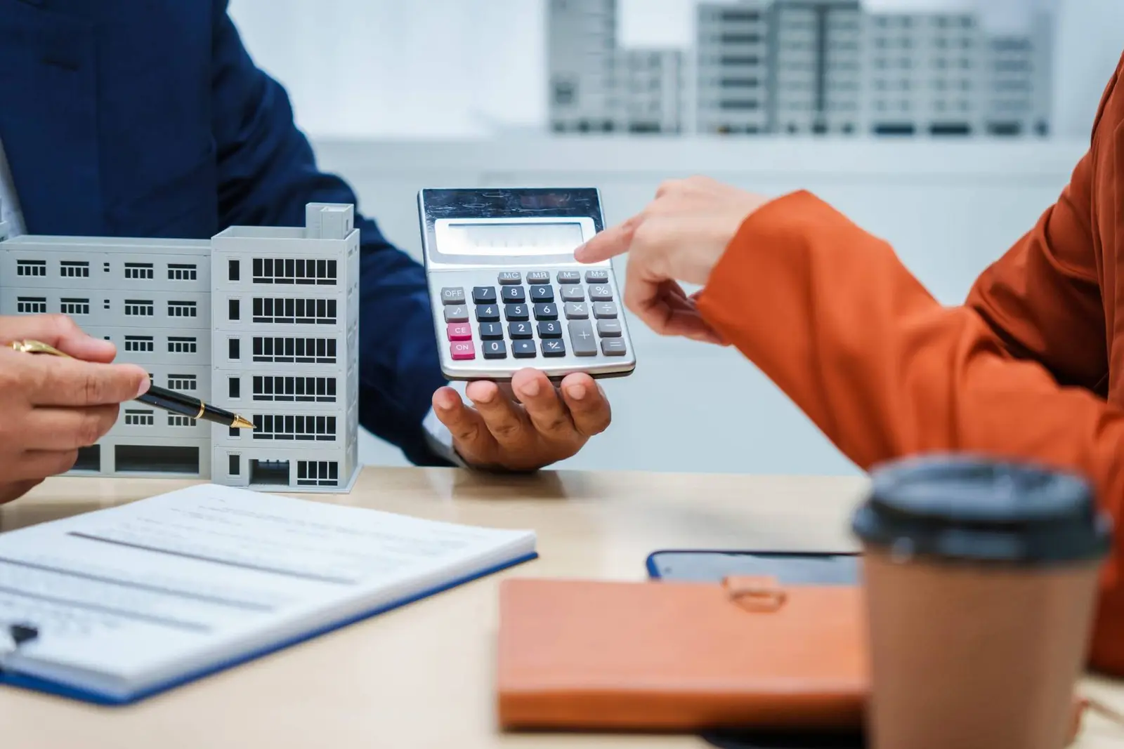 Two people at a desk with a calculator and a scale model of an office building